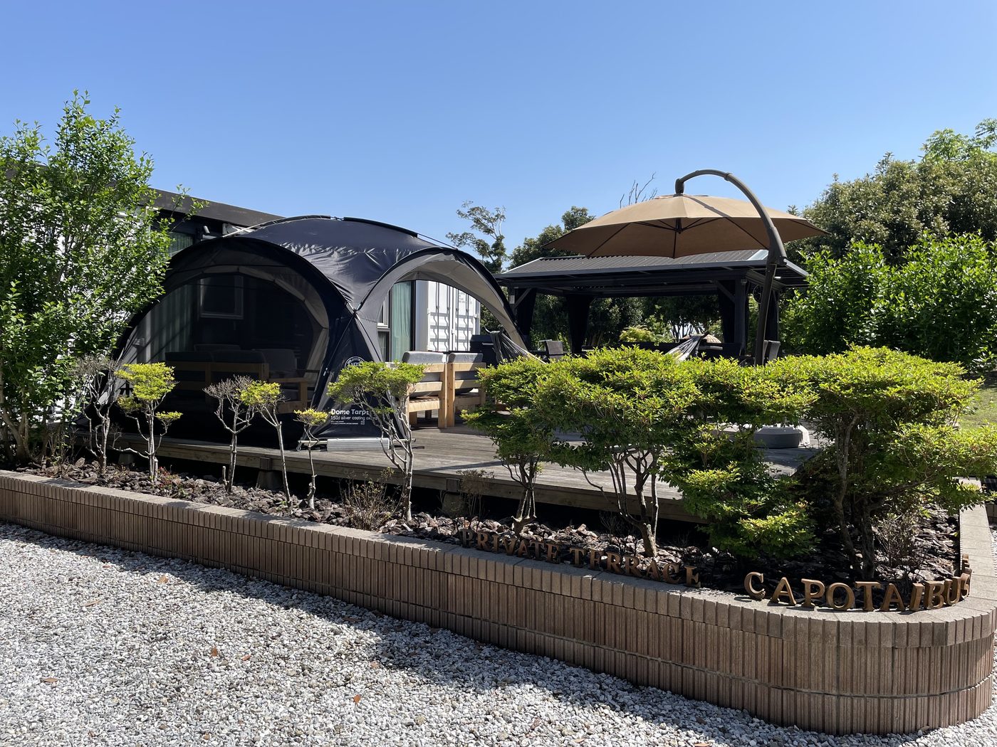 植栽の奥にドームテントとガゼボ、手前に PRIVATE THRACE CAPO TAIBUSA の看板